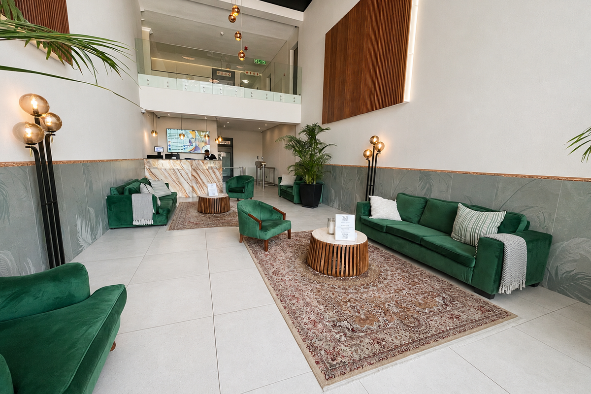 A spacious, modern double-volume lobby or lounge area featuring high ceilings, tiled floors, and a mezzanine level with a glass balustrade.
