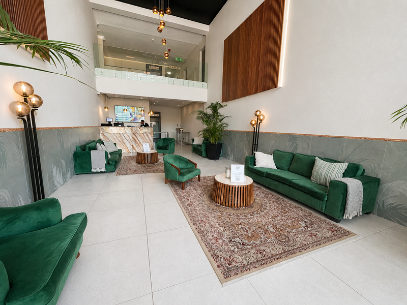 A spacious, modern double-volume lobby or lounge area featuring high ceilings, tiled floors, and a mezzanine level with a glass balustrade.