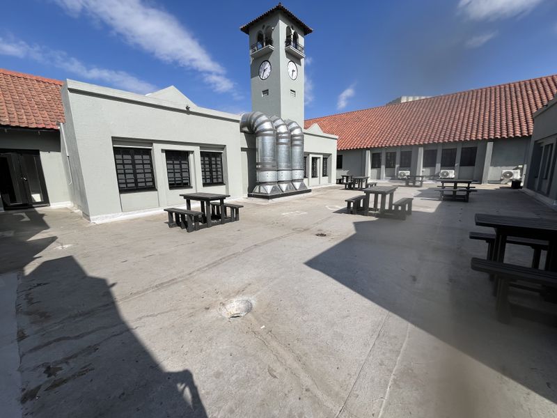 Spacious outdoor courtyard area featuring a prominent clock tower, industrial ventilation systems, and terracotta roof tiling.