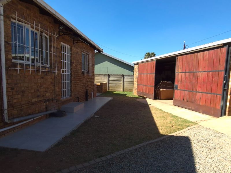 Rear exterior view showing a face brick house, concrete pathway, and a detached garage with timber doors.