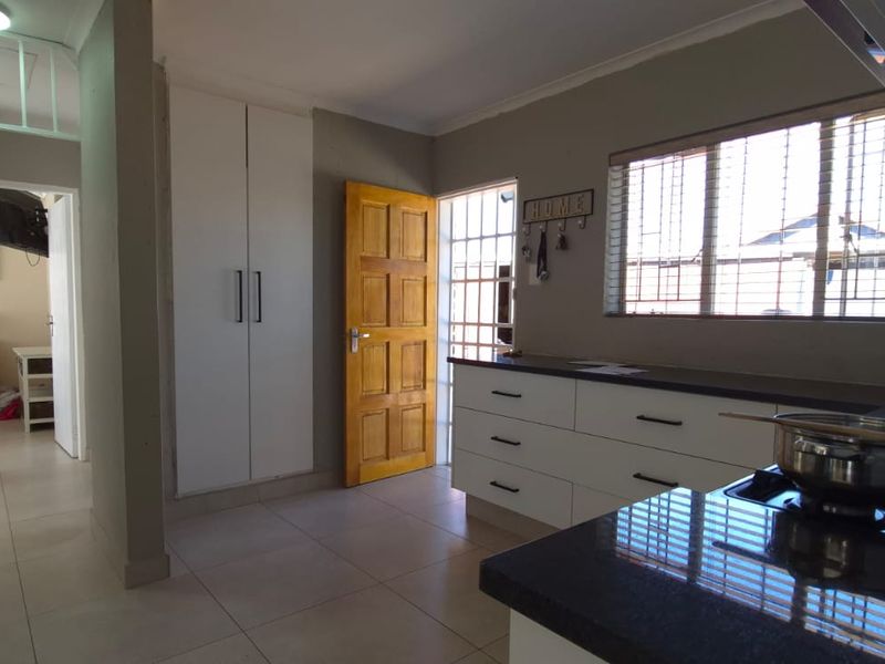 A functional kitchen featuring modern white cabinetry, dark granite countertops, a gas hob, and tiled flooring, with direct access to the hallway.
