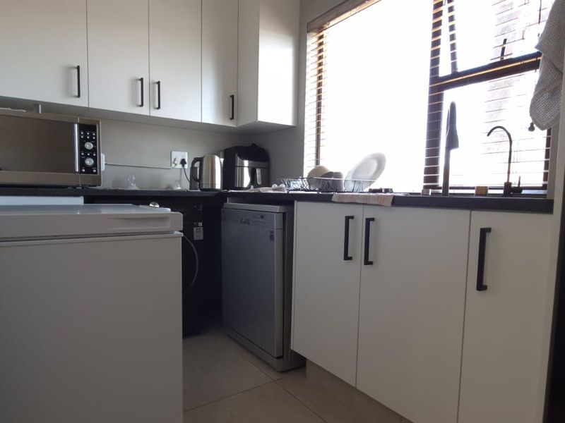 A functional kitchen featuring white cabinetry, dark countertops, and a window with blinds, providing a practical workspace with integrated storage.