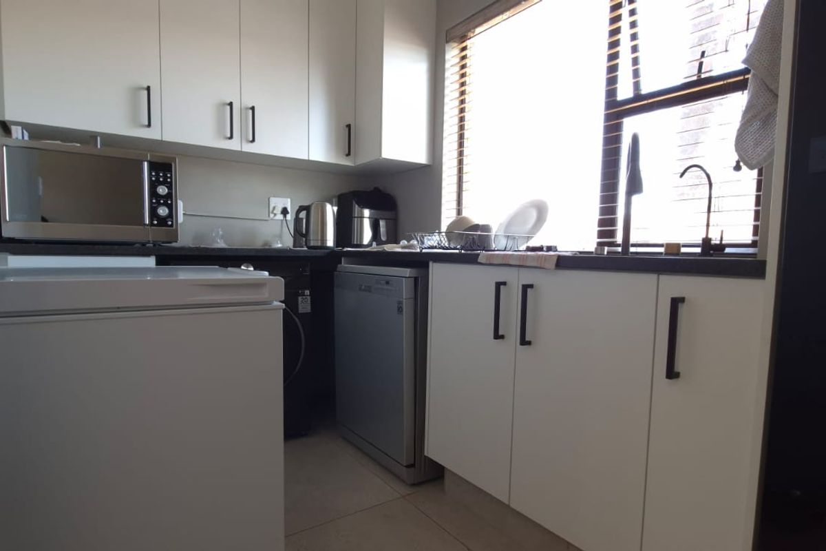 A functional kitchen featuring white cabinetry, dark countertops, and a window with blinds, providing a practical workspace with integrated storage.