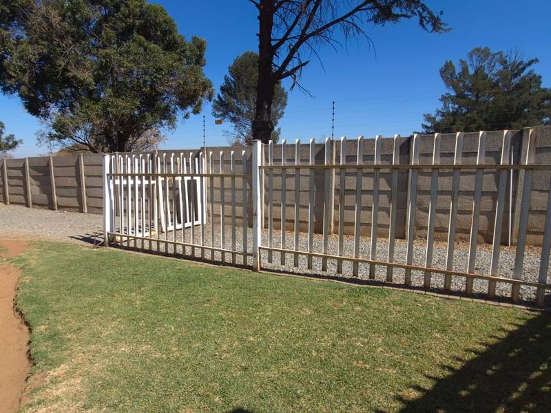 A view of the rear yard featuring a lawn area, gravel path, and perimeter security fencing with a concrete boundary wall.