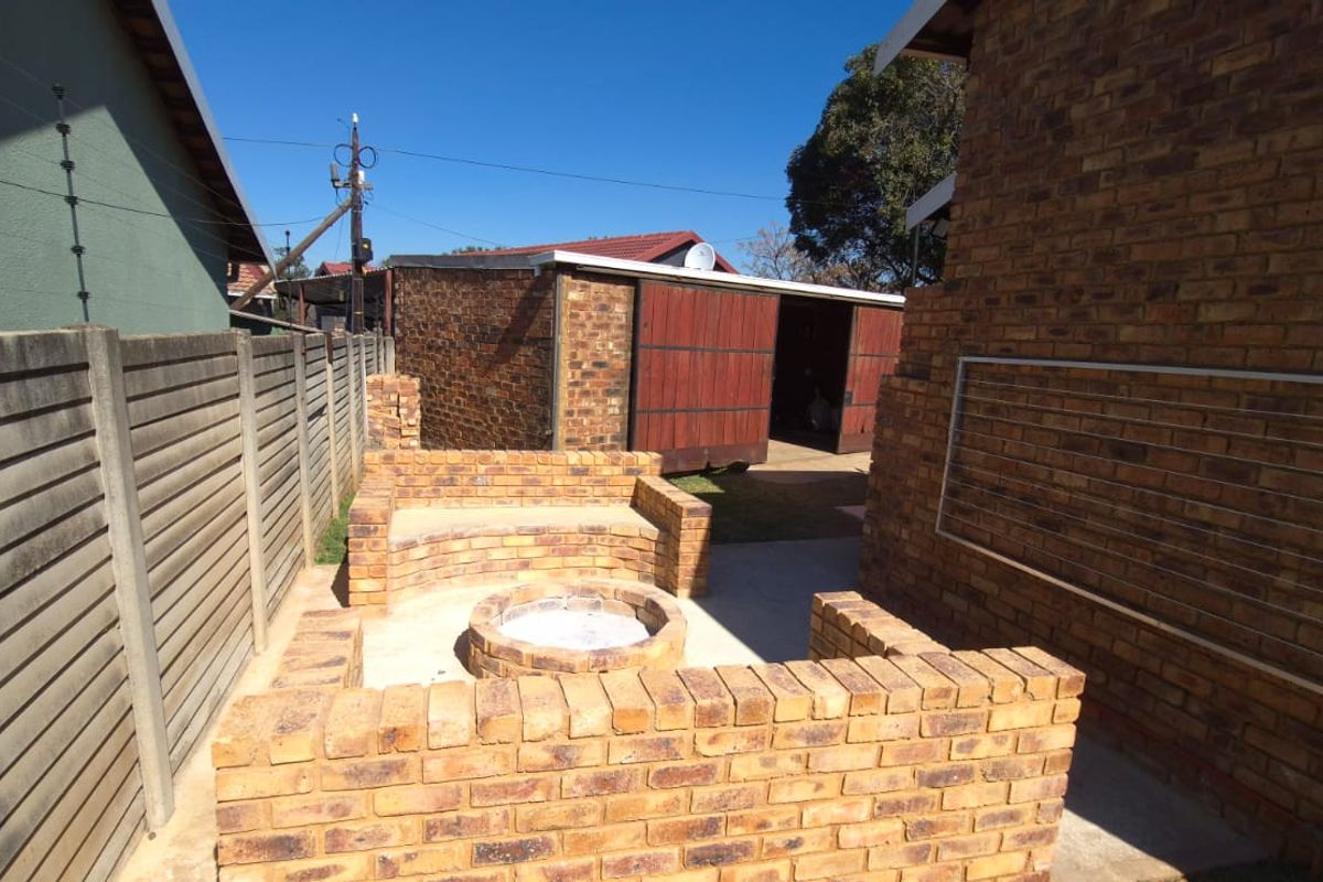 Rear outdoor area featuring a built-in brick fire pit with integrated seating, enclosed by a precast concrete boundary wall and adjacent to a brick garage.