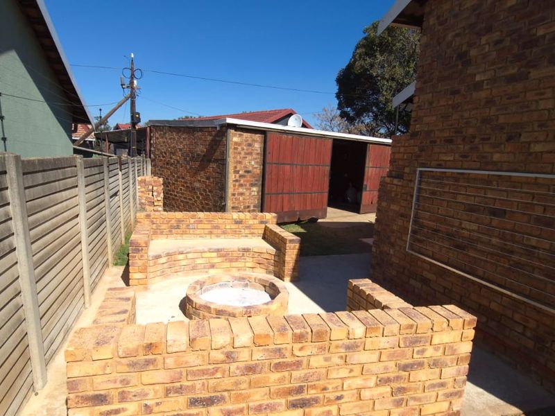 Rear outdoor area featuring a built-in brick fire pit with integrated seating, enclosed by a precast concrete boundary wall and adjacent to a brick garage.