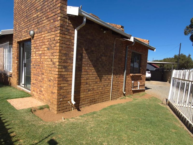 Rear view of the face brick house featuring a lawn area, metal security fencing, and access to the driveway.