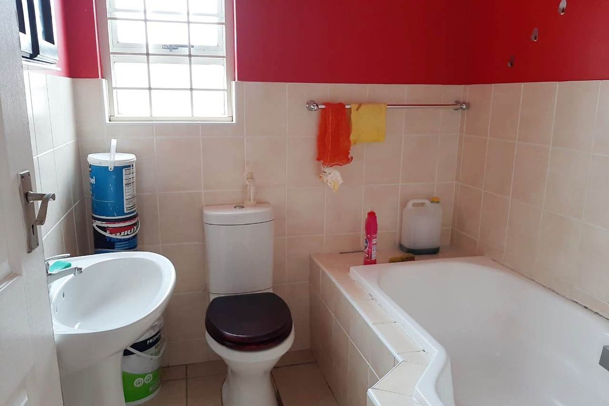 A functional bathroom featuring a built-in bathtub, pedestal basin, and toilet, with tiled finishes and a window for natural light.