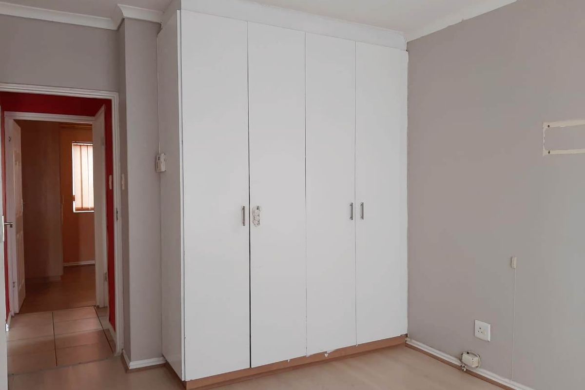 A bedroom featuring a large white built-in wardrobe, neutral wall paint, and laminate flooring, offering a clean and functional space.