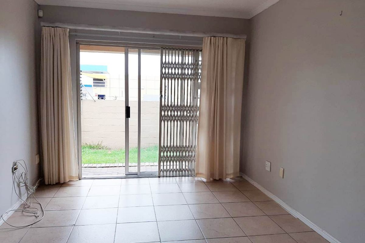 A bright, empty living room featuring tiled flooring and a sliding glass door with a security gate, providing direct access to the rear garden.