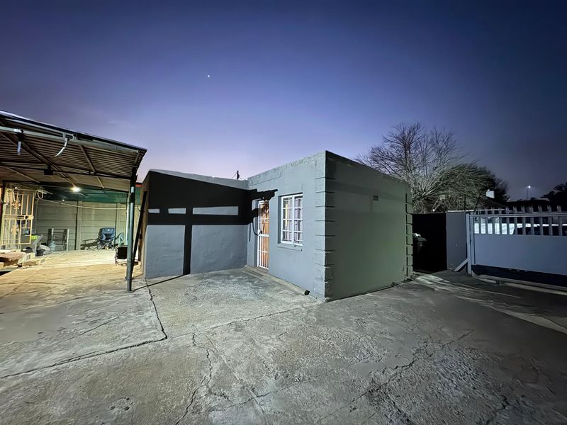 Rear exterior view of the property featuring a concrete driveway, covered patio area, and secure perimeter walling under a twilight sky.