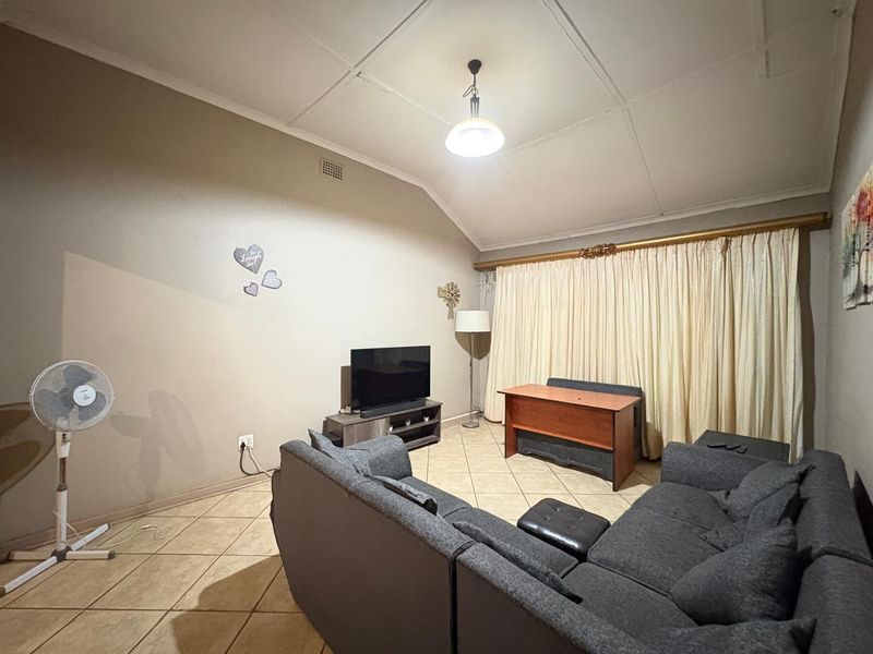 A living room featuring tiled flooring and a vaulted ceiling with visible paneling, offering a functional space ready for modernization.