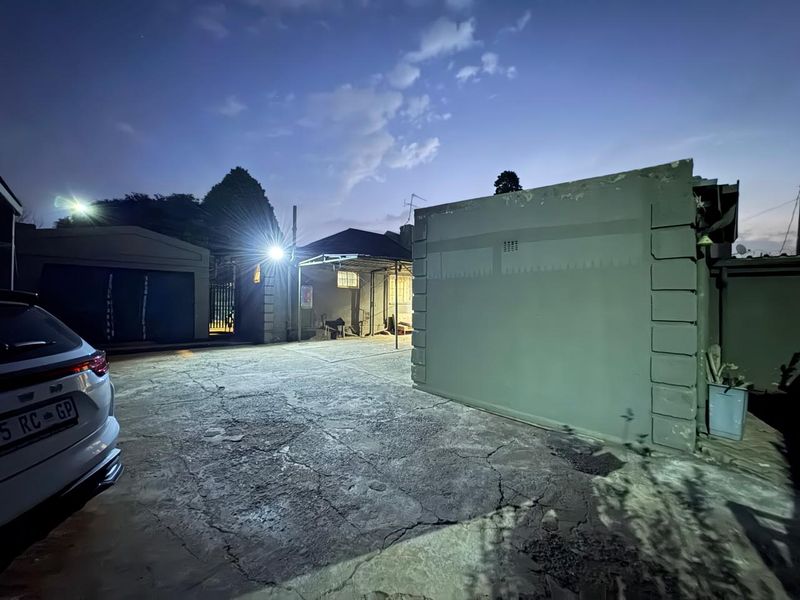 Rear exterior view of the property featuring a concrete driveway, carport, and security lighting at dusk.