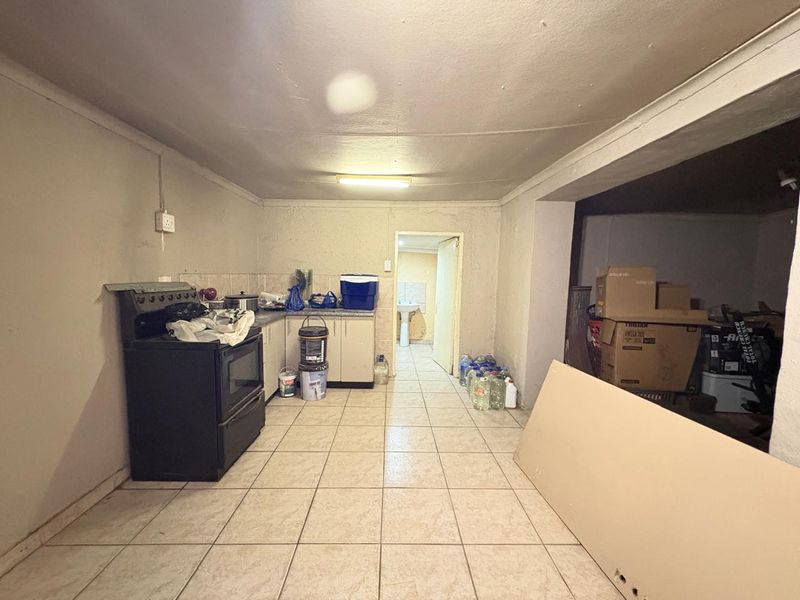 A functional kitchen area featuring tiled flooring, built-in cabinetry, and a freestanding stove, leading through to an adjacent utility or bathroom space.
