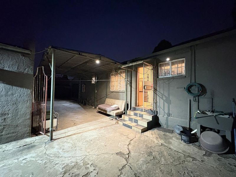 Rear exterior view of the property featuring a covered carport, concrete paving, security gate, and external wash basin area.