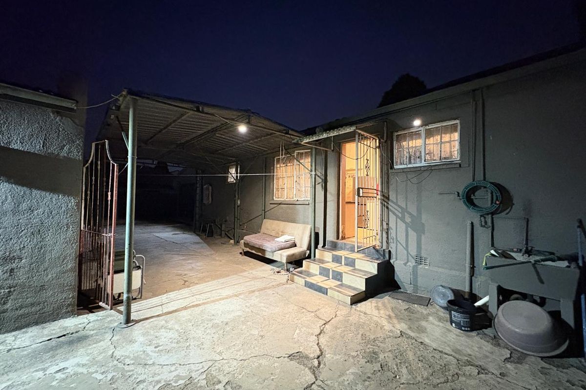 Rear exterior view of the property featuring a covered carport, concrete paving, security gate, and external wash basin area.