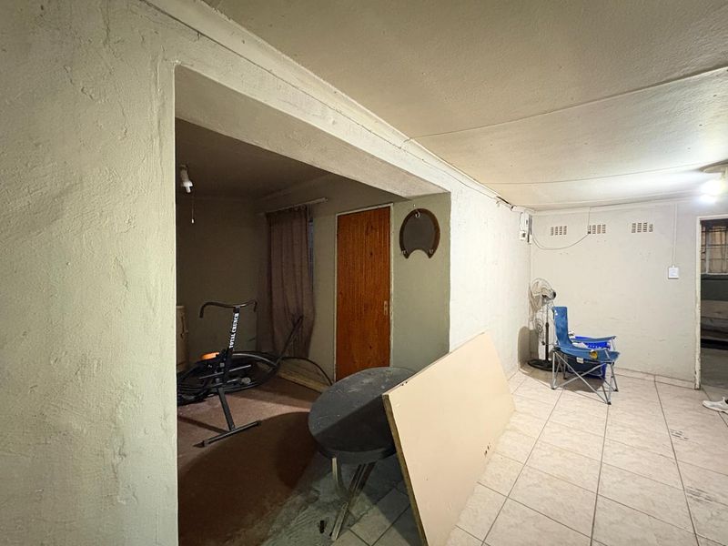 An interior living space featuring tiled flooring and a timber door, currently in need of cosmetic renovation and wall repairs.
