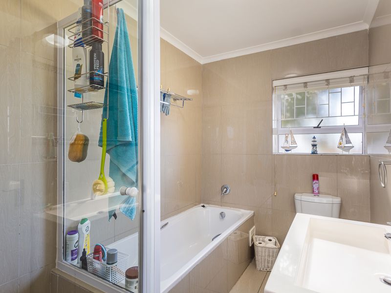 A functional bathroom featuring a bathtub, shower enclosure, vanity basin, and toilet, finished with neutral wall and floor tiles.