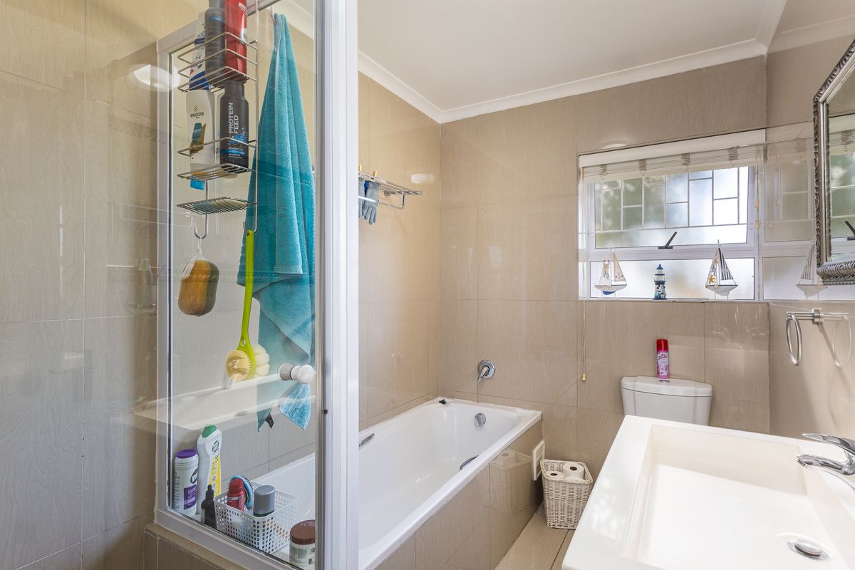A functional bathroom featuring a bathtub, shower enclosure, vanity basin, and toilet, finished with neutral wall and floor tiles.