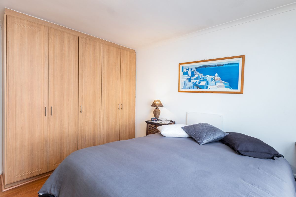 A well-maintained bedroom featuring light wood-toned built-in wardrobes and laminate flooring, offering a clean and functional living space.