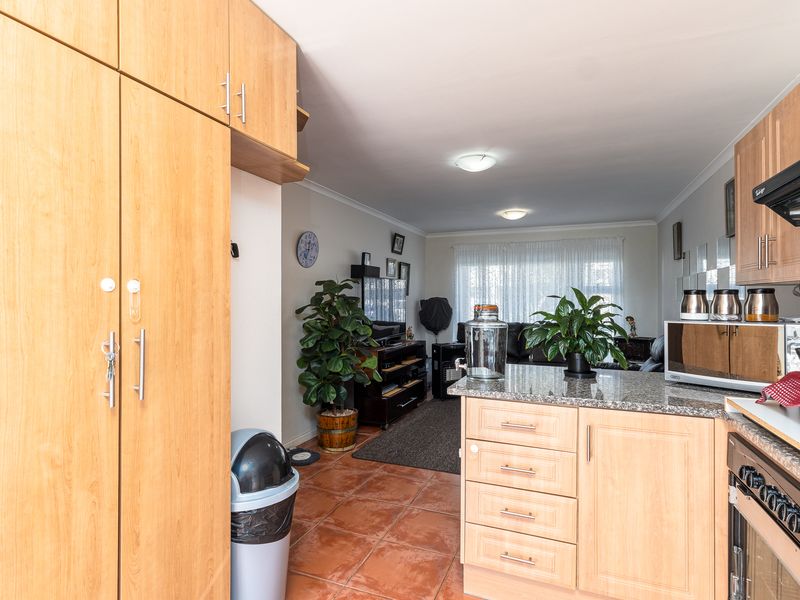 Open-plan kitchen and living area featuring light wood cabinetry, granite countertops, built-in oven, extractor fan, and tiled flooring throughout.