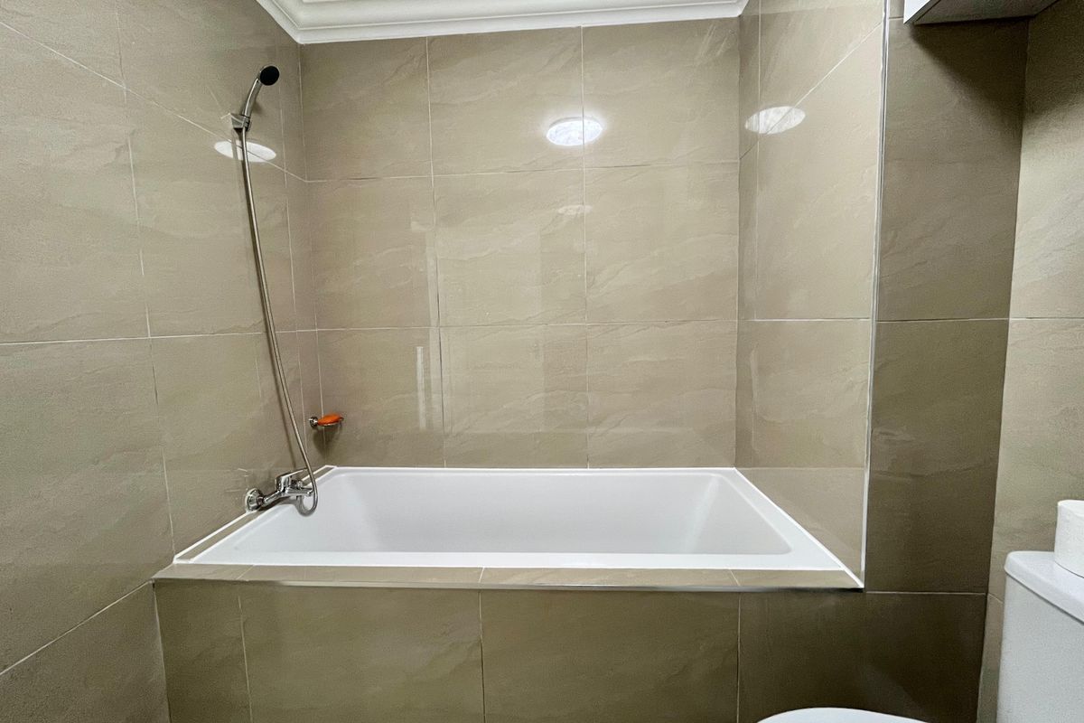 A clean, modern bathroom featuring a built-in bathtub with a handheld shower attachment and neutral ceramic wall tiling.