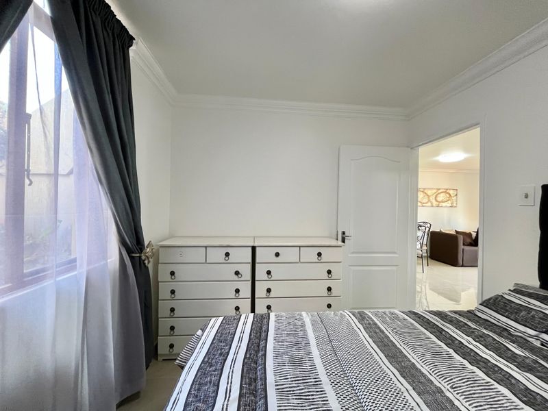 A well-maintained bedroom featuring neutral walls, crown molding, and a window with curtains, offering a view into the adjacent living area.