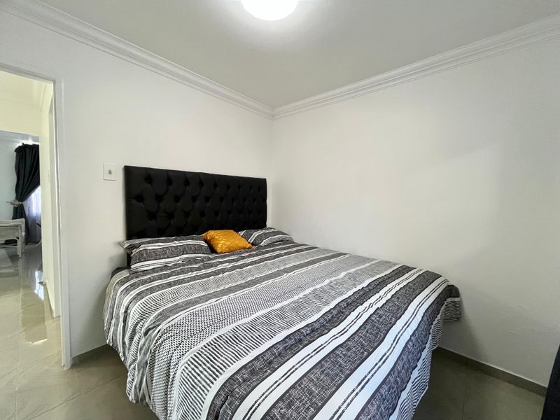 A clean and simple bedroom featuring neutral tiled flooring, white walls, and decorative ceiling cornicing, providing a functional and well-maintained living space.
