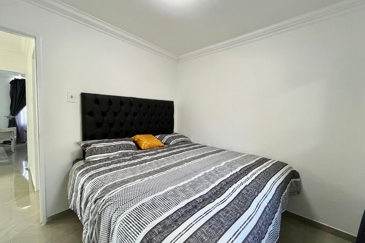 A clean and simple bedroom featuring neutral tiled flooring, white walls, and decorative ceiling cornicing, providing a functional and well-maintained living space.