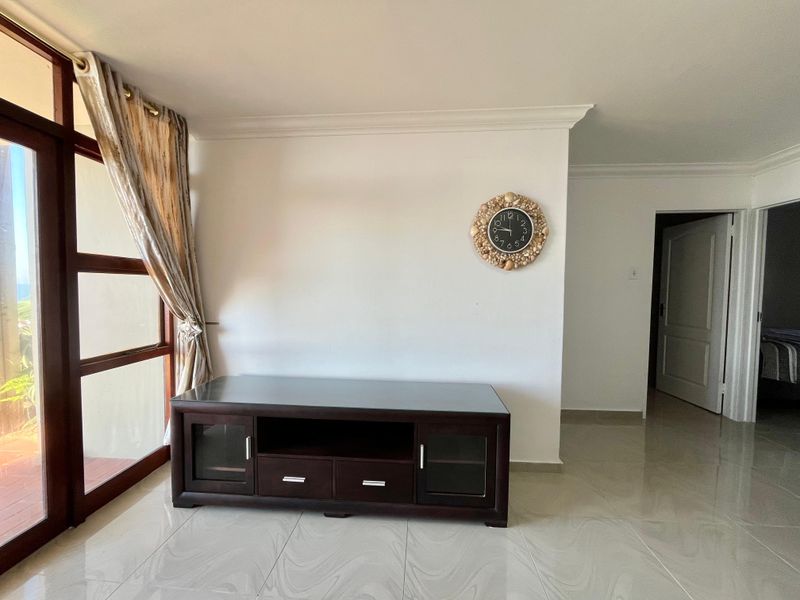 A bright living area featuring polished tiled flooring, coving, and a timber-framed glass door providing access to an outdoor space.
