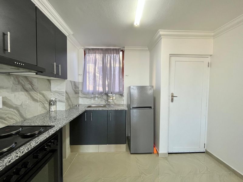 Modern kitchen featuring dark cabinetry, granite countertops, tiled flooring, and integrated appliances, offering a clean and functional cooking space.