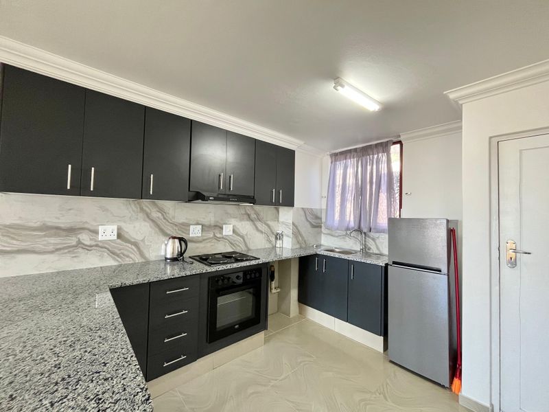 Modern kitchen featuring dark cabinetry, granite countertops, marble-effect splashback, built-in oven, electric hob, and integrated sink with ample storage space.
