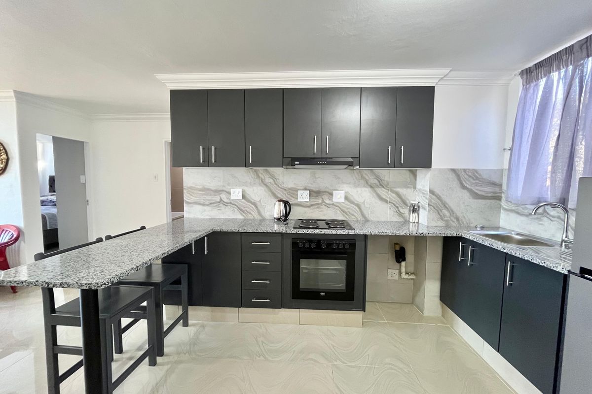 Modern kitchen featuring dark cabinetry, granite countertops, a breakfast bar, built-in oven, electric hob, and stylish marble-effect splashback.