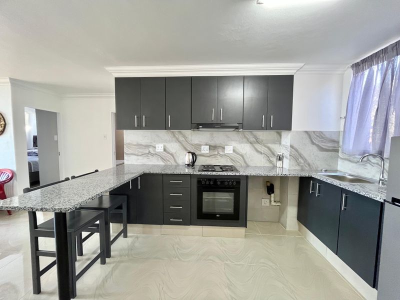 Modern kitchen featuring dark cabinetry, granite countertops, a breakfast bar, built-in oven, electric hob, and stylish marble-effect splashback.