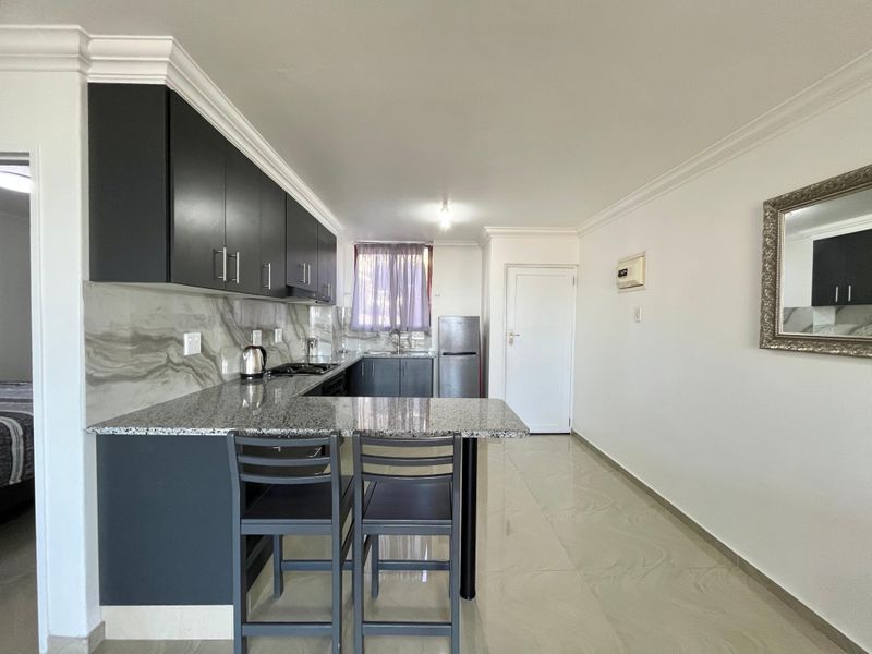 Modern kitchen featuring dark cabinetry, granite countertops, a breakfast bar, and marble-effect splashback, complemented by neutral tiled flooring and clean finishes.