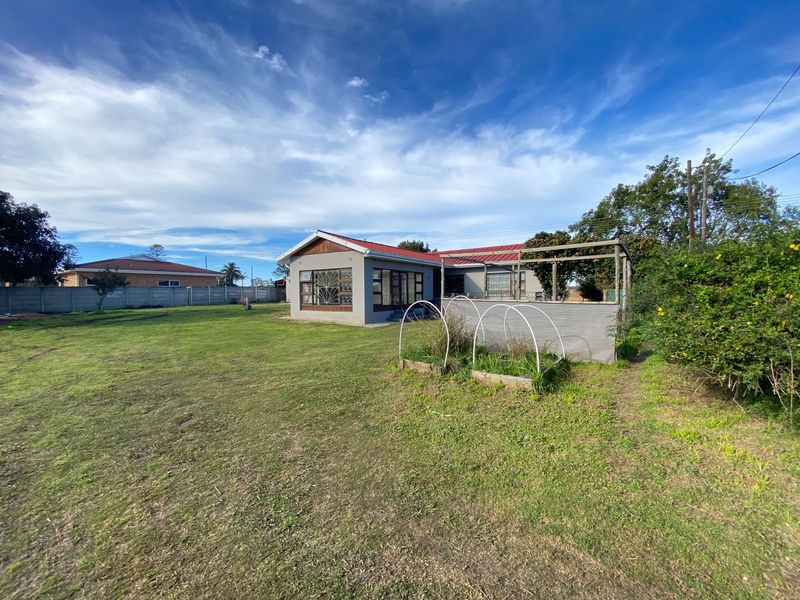 Rear view of the property featuring a metal roof, aluminium windows with security bars, and a timber pergola structure set within a large garden.