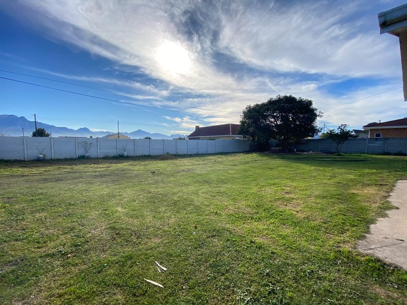 A spacious, open backyard featuring a large lawn area enclosed by a precast concrete boundary wall with mountain views in the distance.