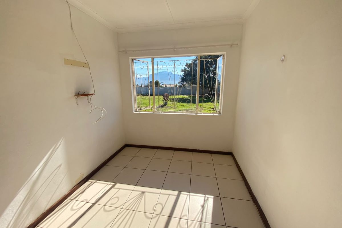 An empty bedroom featuring tiled flooring and a window with security bars, offering a view of the garden and mountains.