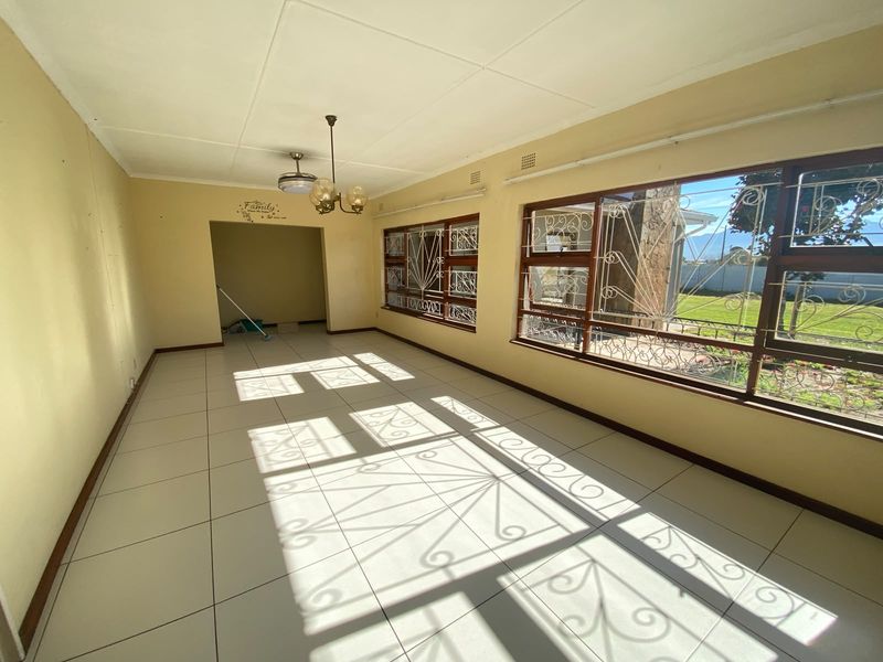 A spacious, empty living room featuring tiled flooring, large windows with security bars, and natural light, offering a blank canvas for renovation.