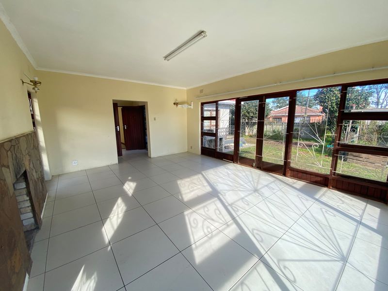 Spacious, empty living room featuring tiled flooring, a stone-clad fireplace, and large timber-framed glass doors providing direct access to the garden.