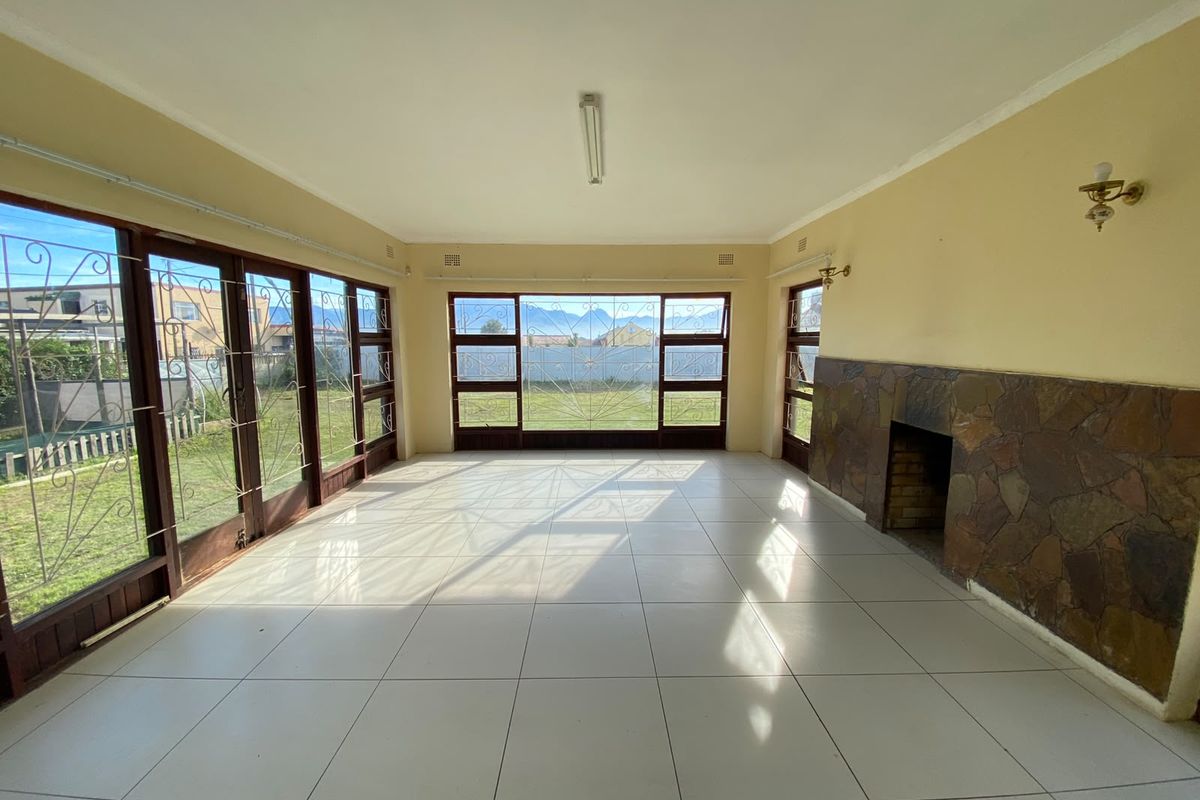 Spacious, light-filled living room featuring large windows with garden views, tiled flooring, and a stone-clad fireplace.
