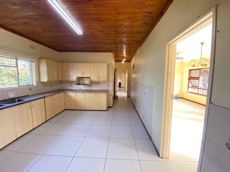 A functional kitchen featuring laminate cabinetry, tiled flooring, and a timber ceiling, with an open doorway leading to an adjacent living area.