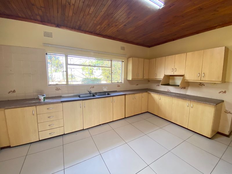 A spacious, empty kitchen featuring light wood-look cabinetry, laminate countertops, a double basin sink, and a distinctive timber-paneled ceiling.