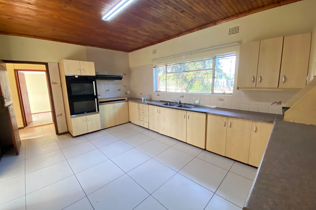 A spacious, empty kitchen featuring light wood cabinetry, a built-in double oven, tiled flooring, and a timber-paneled ceiling.