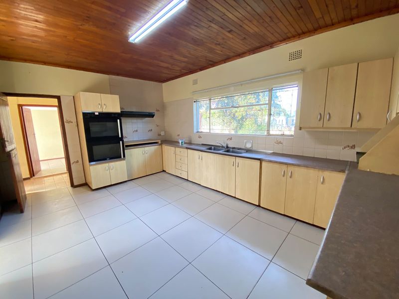 A spacious, empty kitchen featuring light wood cabinetry, a built-in double oven, tiled flooring, and a timber-paneled ceiling.