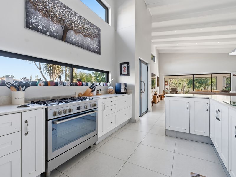 Modern open-plan kitchen featuring white shaker cabinetry, stone countertops, gas range, and high ceilings with exposed beams, flowing into the living area.