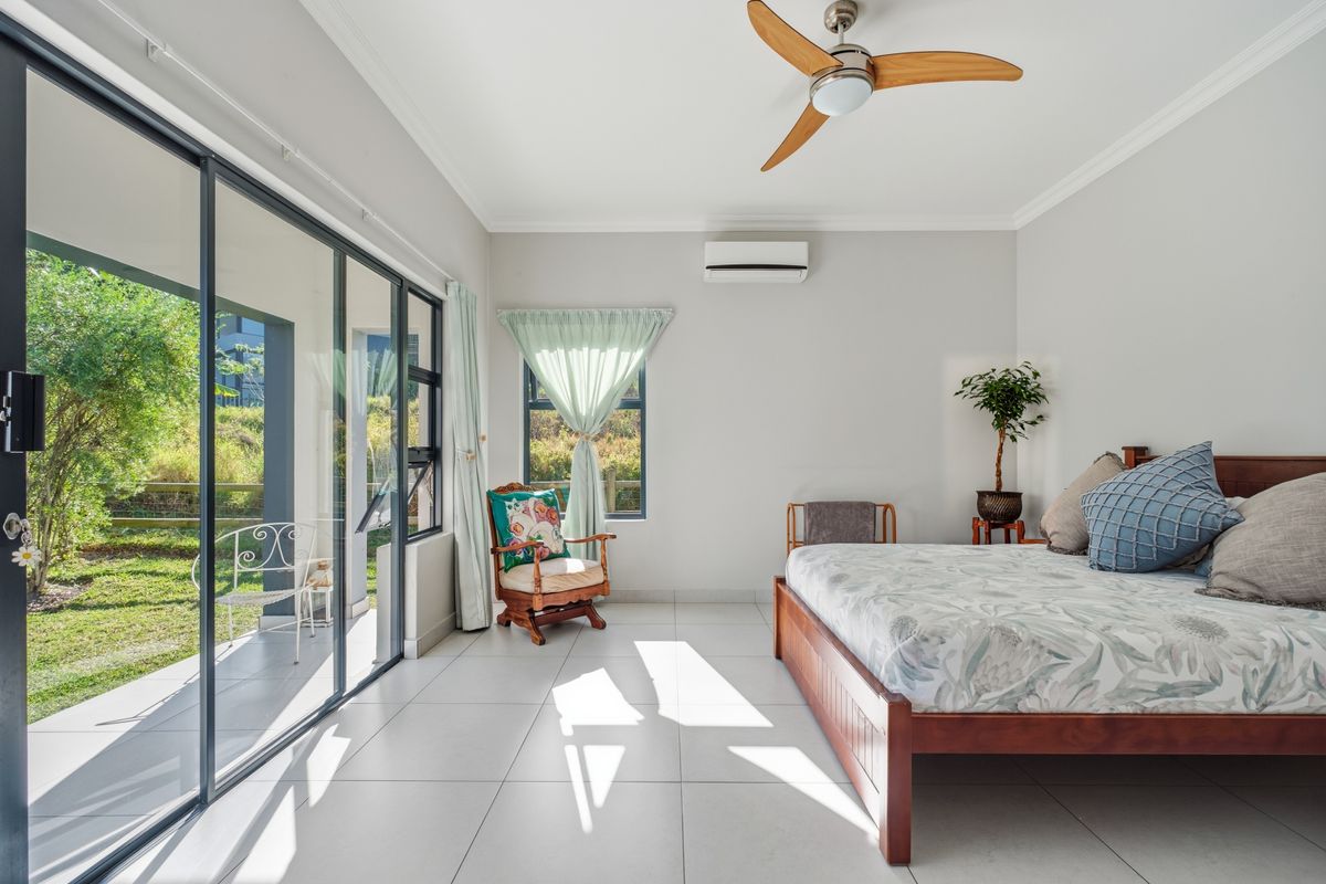 A bright and spacious bedroom featuring tiled flooring, a ceiling fan, split-system air conditioning, and large sliding glass doors providing direct access to the garden.