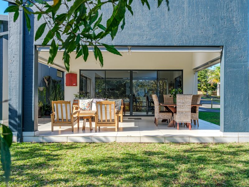 A covered outdoor patio featuring tiled flooring, a retractable awning, and direct access to the interior through large sliding glass doors.