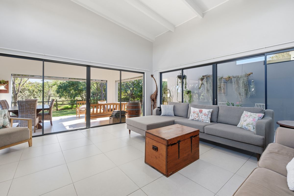 Spacious living room featuring large sliding glass doors that provide seamless indoor-outdoor flow, tiled flooring, and an airy exposed beam ceiling.