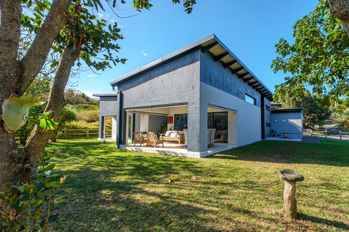 A modern rear elevation featuring a covered patio with large sliding glass doors, overlooking a well-maintained garden and lawn area.